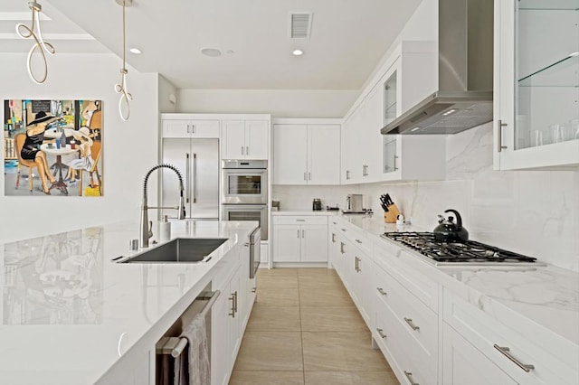 kitchen featuring stainless steel appliances, hanging light fixtures, wall chimney range hood, white cabinets, and sink