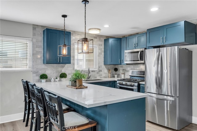 kitchen featuring a kitchen breakfast bar, appliances with stainless steel finishes, blue cabinets, and pendant lighting