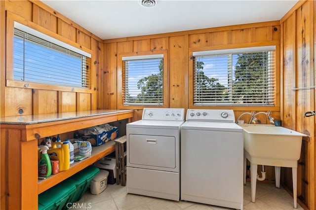 clothes washing area with light tile patterned floors, washer and clothes dryer, and wooden walls