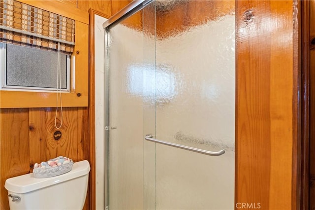 bathroom featuring a shower with shower door, toilet, and wood walls