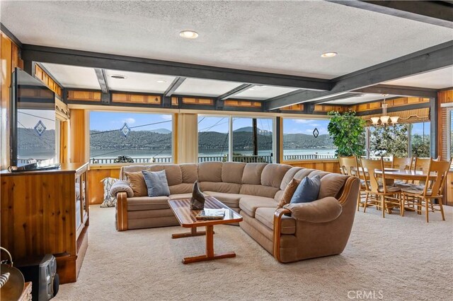 carpeted living room with beam ceiling, an inviting chandelier, a water and mountain view, and a textured ceiling