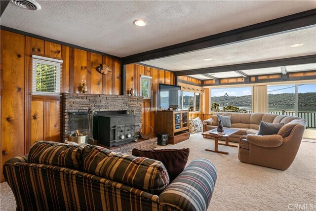 living room with wood walls, a fireplace, a textured ceiling, carpet flooring, and beam ceiling