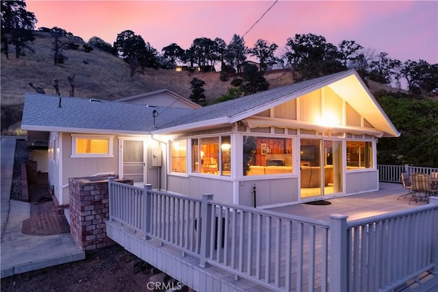 back house at dusk with a wooden deck and a sunroom