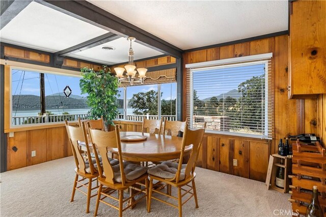 dining room featuring an inviting chandelier, wooden walls, a water view, carpet floors, and beam ceiling