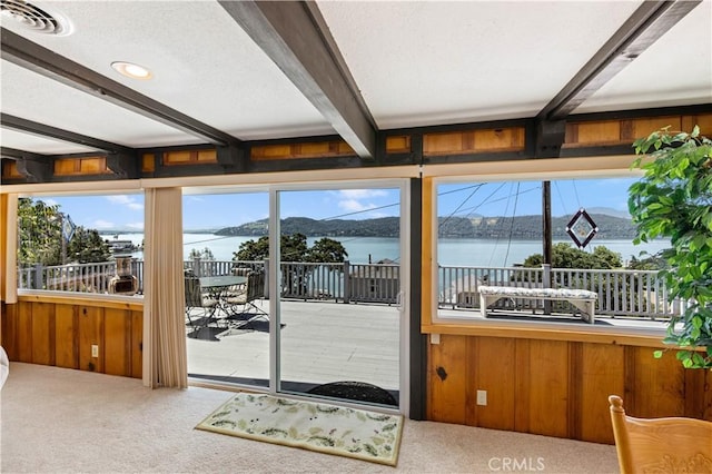 doorway to outside featuring a water and mountain view, carpet, wood walls, and beamed ceiling