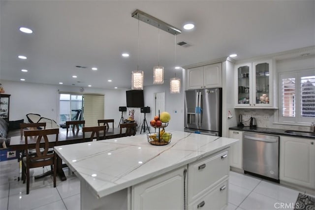 kitchen featuring decorative light fixtures, appliances with stainless steel finishes, white cabinetry, and a center island