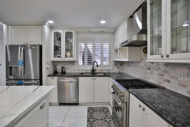 kitchen featuring white cabinets, wall chimney exhaust hood, stainless steel appliances, dark stone countertops, and sink