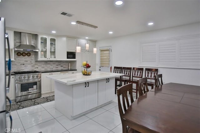 kitchen featuring stainless steel appliances, hanging light fixtures, a kitchen island, wall chimney exhaust hood, and white cabinets