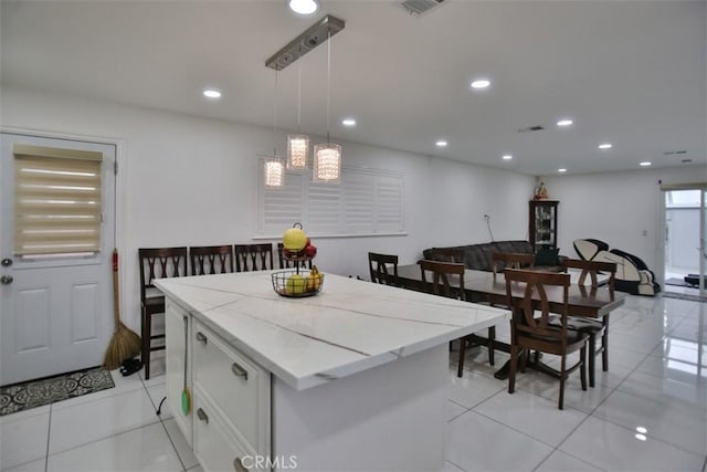 kitchen with pendant lighting, white cabinets, a center island, light tile patterned flooring, and light stone counters