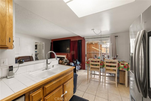 kitchen featuring pendant lighting, sink, stainless steel fridge, tile countertops, and light tile patterned floors