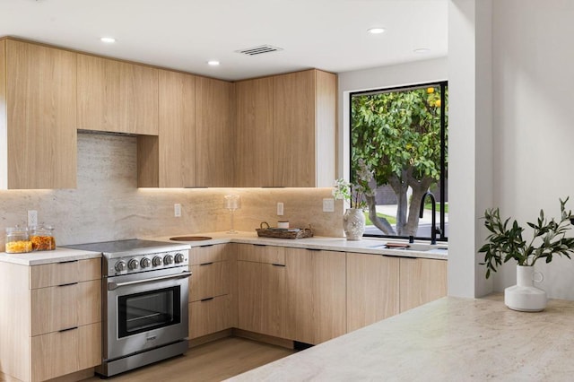 kitchen with decorative backsplash, stainless steel electric range oven, light brown cabinets, and sink