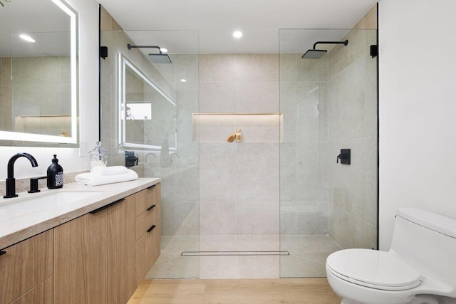 bathroom with toilet, vanity, hardwood / wood-style floors, and a tile shower