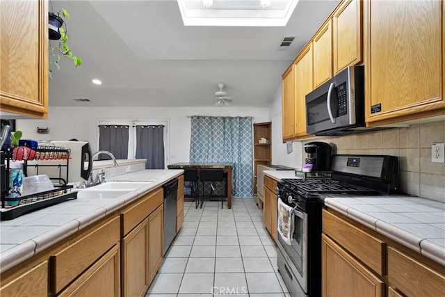 kitchen with light tile patterned floors, a skylight, tile countertops, appliances with stainless steel finishes, and sink