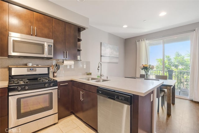 kitchen with appliances with stainless steel finishes, tasteful backsplash, sink, kitchen peninsula, and light tile patterned floors