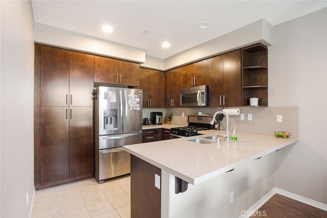 kitchen featuring a kitchen bar, kitchen peninsula, stainless steel appliances, dark brown cabinets, and sink