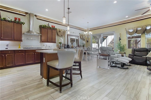 kitchen with a kitchen island, wall chimney range hood, a kitchen breakfast bar, hanging light fixtures, and crown molding