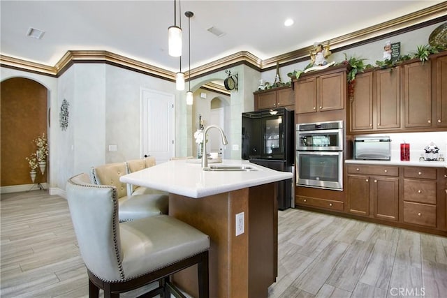 kitchen featuring a center island with sink, sink, crown molding, and pendant lighting