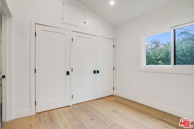 unfurnished bedroom featuring vaulted ceiling, light hardwood / wood-style floors, and a closet