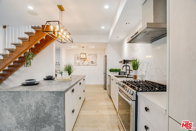 kitchen with appliances with stainless steel finishes, white cabinetry, light hardwood / wood-style floors, decorative light fixtures, and exhaust hood