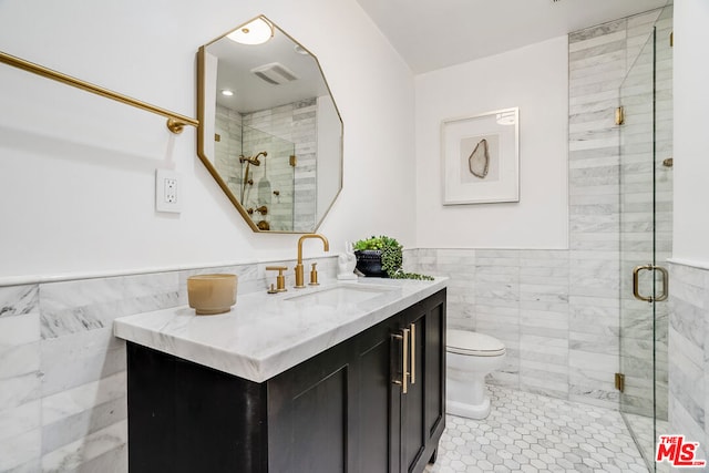 bathroom with vanity, toilet, a shower with door, and tile walls