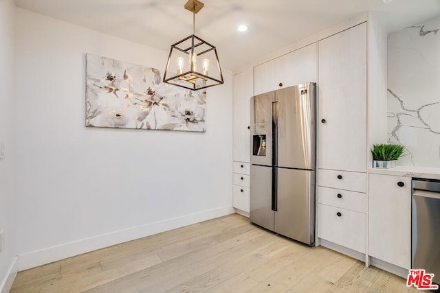 kitchen featuring white cabinets, stainless steel appliances, hanging light fixtures, and light wood-type flooring