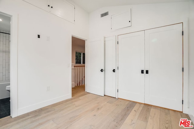 unfurnished bedroom featuring ensuite bathroom, high vaulted ceiling, light wood-type flooring, and a closet