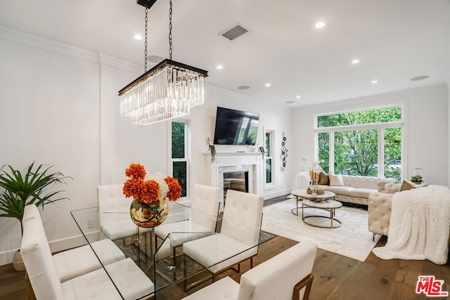 dining space with a notable chandelier, crown molding, wood-type flooring, and a high end fireplace