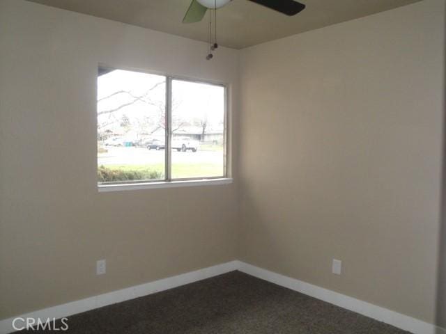 spare room with ceiling fan and dark colored carpet