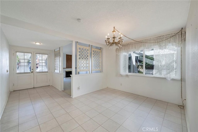 tiled empty room with a notable chandelier, a wealth of natural light, and a textured ceiling