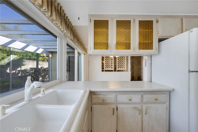 kitchen with white refrigerator, light brown cabinetry, and sink