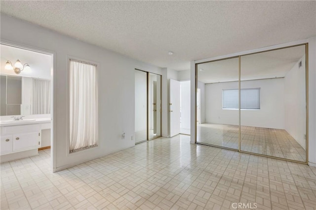 unfurnished bedroom featuring a textured ceiling, multiple closets, connected bathroom, and sink