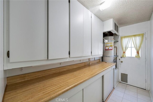 kitchen featuring light tile patterned floors, strapped water heater, white cabinetry, and a textured ceiling