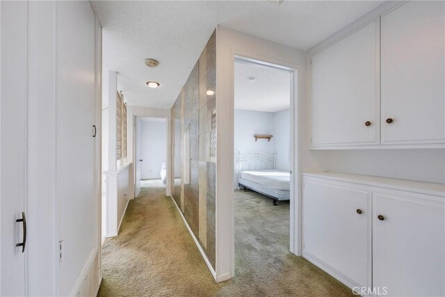 corridor with light colored carpet and a textured ceiling