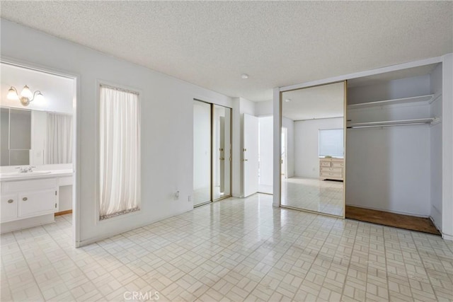 unfurnished bedroom with a textured ceiling, sink, two closets, and ensuite bath