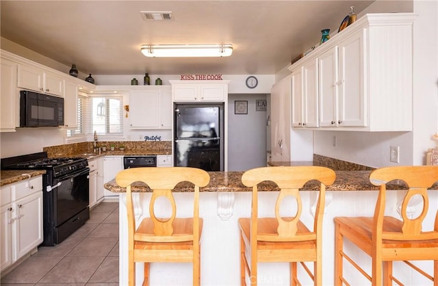 kitchen featuring a kitchen bar, white cabinets, dark stone counters, and black appliances