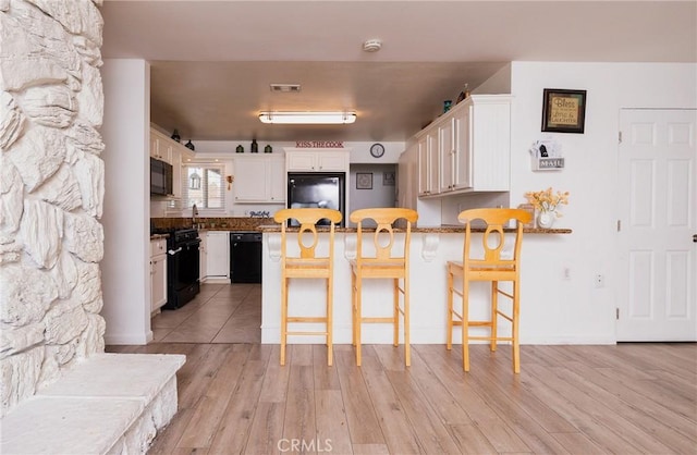 kitchen featuring black appliances, a breakfast bar area, and white cabinetry