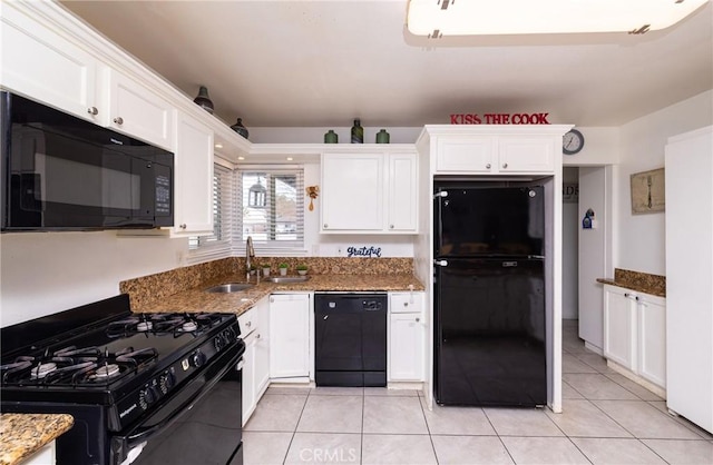 kitchen featuring dark stone countertops, black appliances, sink, light tile patterned flooring, and white cabinetry