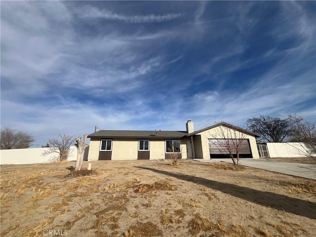 back of house featuring fence, concrete driveway, stucco siding, a chimney, and an attached garage