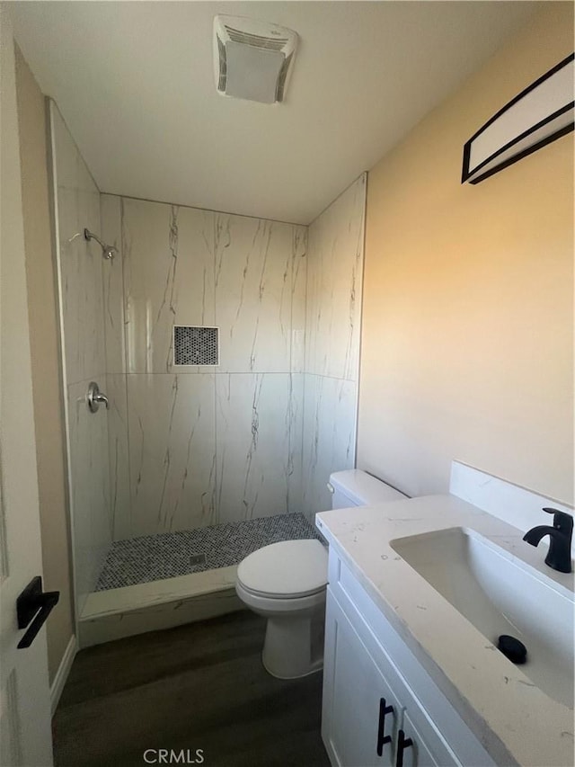 bathroom with toilet, a tile shower, hardwood / wood-style floors, and vanity