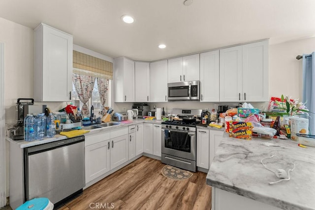 kitchen featuring light stone counters, stainless steel appliances, light wood-type flooring, white cabinets, and sink