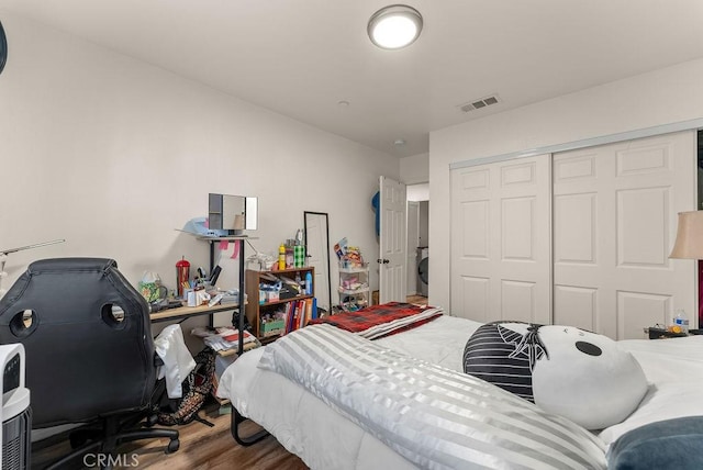 bedroom featuring hardwood / wood-style flooring, stacked washing maching and dryer, and a closet