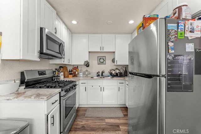 kitchen with stainless steel appliances, light stone counters, dark hardwood / wood-style floors, sink, and white cabinetry