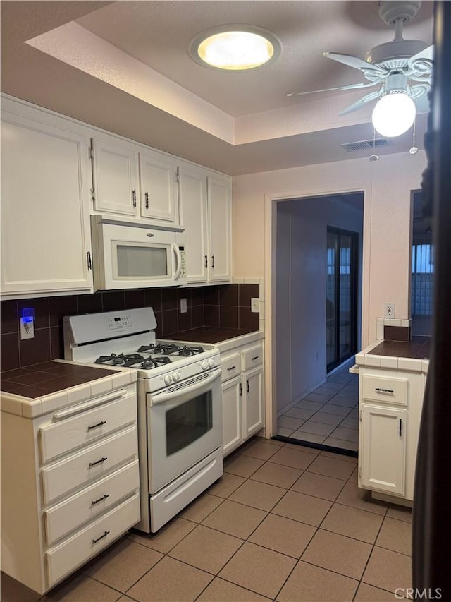 kitchen featuring light tile patterned floors, tile countertops, a tray ceiling, and white appliances