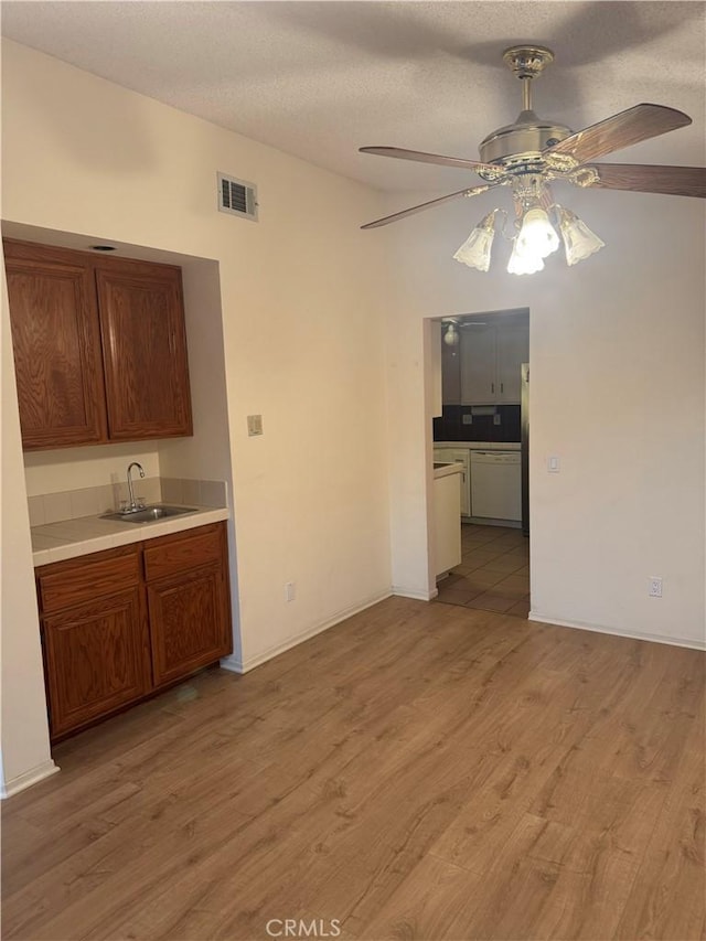 kitchen featuring ceiling fan, sink, a textured ceiling, and light hardwood / wood-style flooring