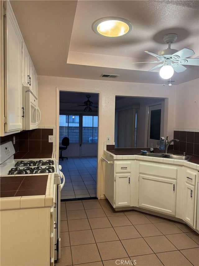 kitchen featuring light tile patterned floors, tile countertops, white cabinetry, white appliances, and sink