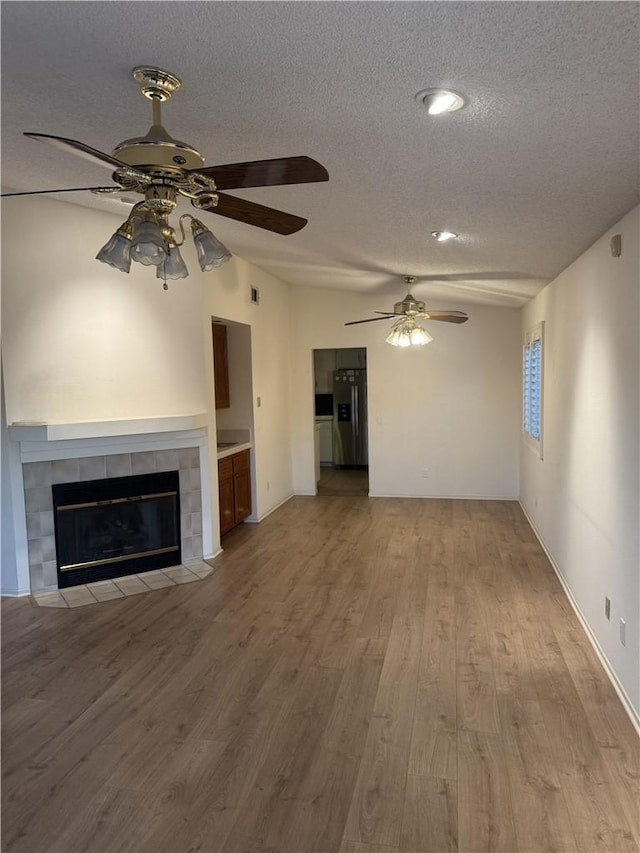 unfurnished living room featuring ceiling fan, a tile fireplace, a textured ceiling, and light hardwood / wood-style flooring