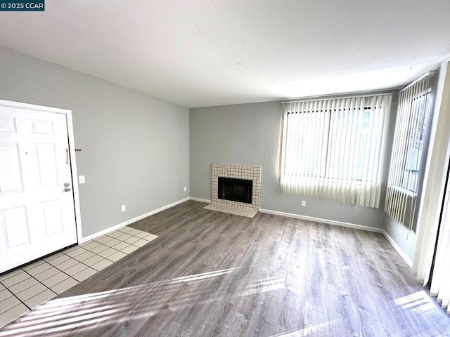 unfurnished living room featuring wood-type flooring and a tiled fireplace