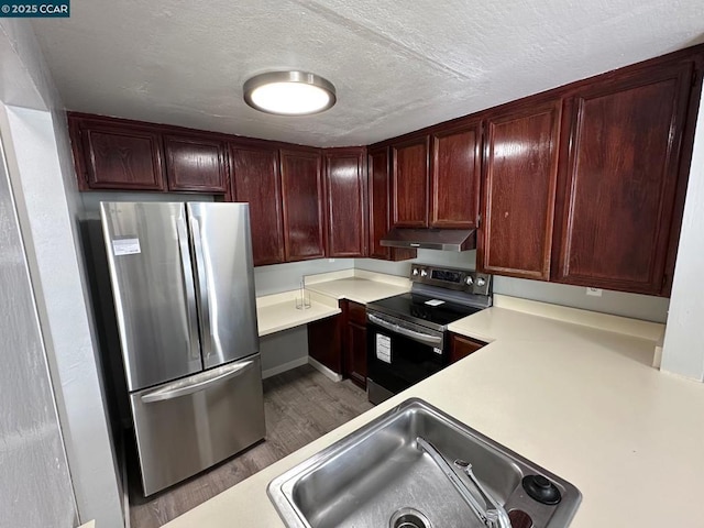 kitchen featuring appliances with stainless steel finishes, hardwood / wood-style floors, built in desk, sink, and a textured ceiling