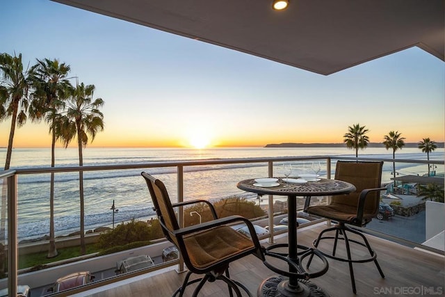 balcony at dusk featuring a view of the beach and a water view