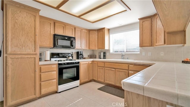 kitchen with tile counters, light brown cabinetry, sink, and white range with gas cooktop